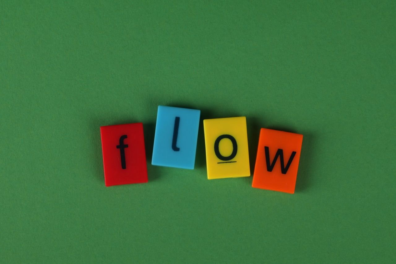 Brightly colored letter tiles spelling 'flow' on green felt backdrop, concept of movement or creativity.